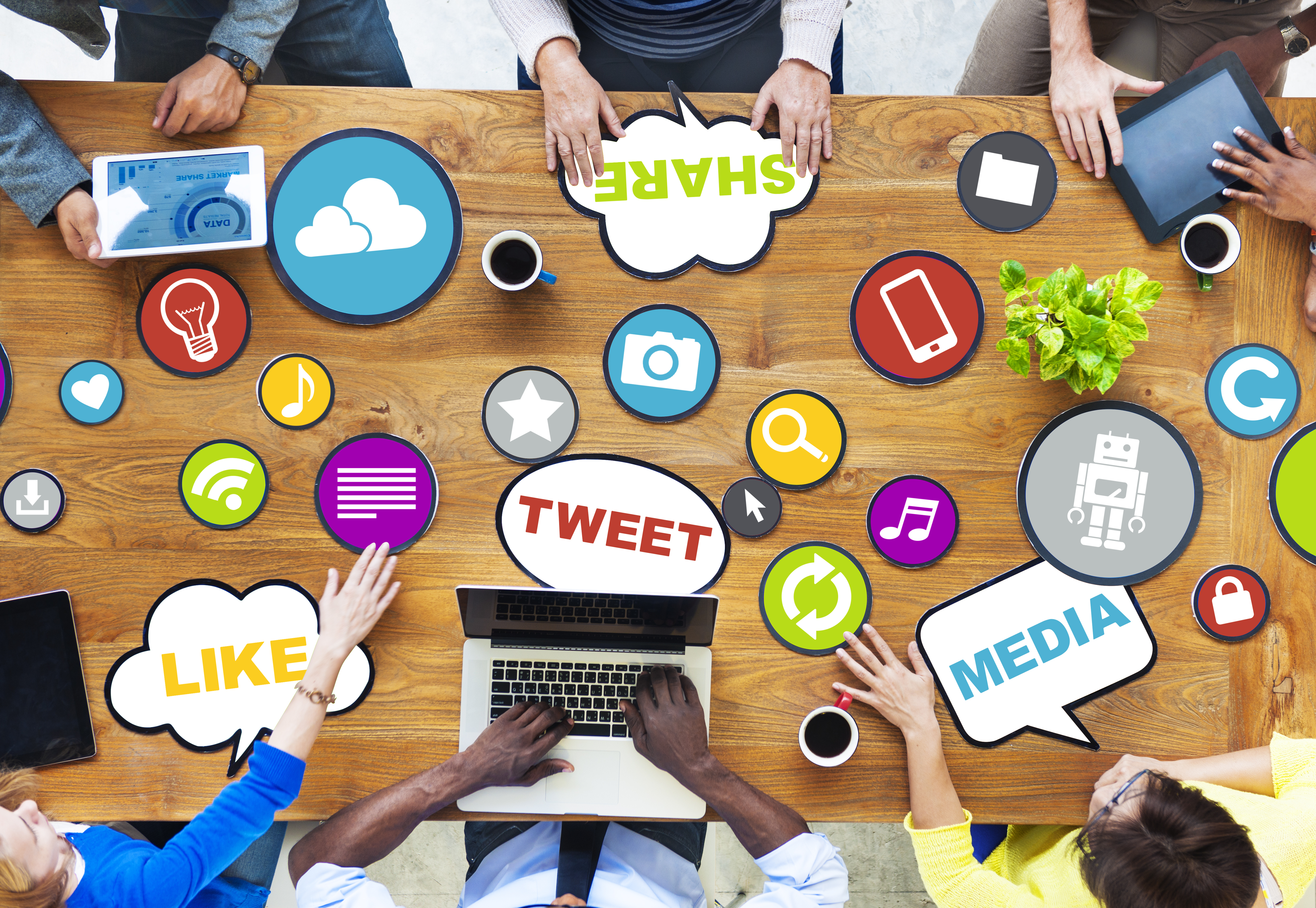 people with tablets and a laptop around a table, table has social media related graphics and words on it